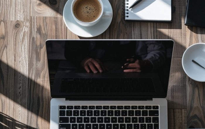 Digital marketing Overhead view of an open laptop, a cup of coffee and a notepad with a pen on a sunlit wooden desk