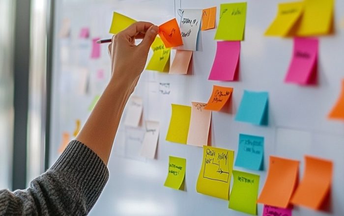 Marketing strategy A hand placing a sticky note on a whiteboard covered with colorful notes and handwritten planning diagrams
